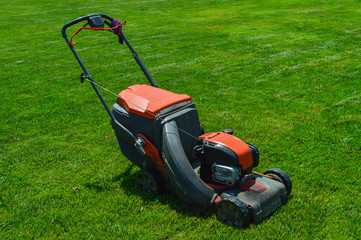 a large lawn mower is standing on the green grass. the device has already tonsured the lawn. gasoline lawn mower ready for use