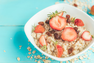 Oatmeal with fresh strawberry and raisins on blue wooden background. Healthy and diet food. Summer breakfast.