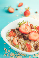Oatmeal with fresh strawberry and raisins on blue wooden background. Healthy and diet food. Summer breakfast.