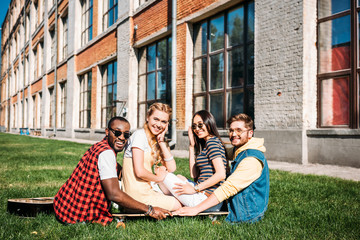 multiracial group of friends looking at camera while sitting on longboard on green grass