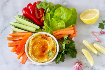 Hummus, different vegetables and lettuce leaves with lemon and garlic on a light background. Vegan food.