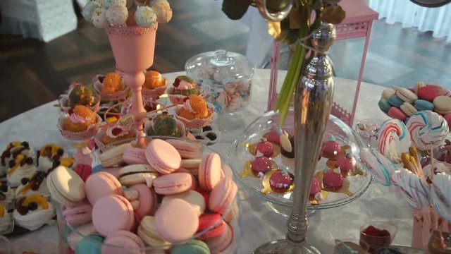 Steadycam shot of the candy bar at wedding. Table is full of different colorful candies, cake-pops, cakes, macarons and cookies.