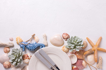  Border from nautical  elements and white plate on white textured  background. Shells, cutlery, sea star, coral, sea horse, succulent echeverial. View from above. Place for text.