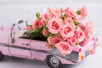 Retro car toy with pink roses flowers against  pink  цршеу textured  wall.