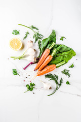 Cooking background with Fresh Vegetables for healthy dinner; carrots, herbs, olive oil, garlic; white marble background flat lay