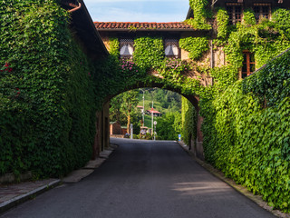 Biella, Italy, June 10, 2018 - Brick house, walls covered with ivy and arch connecting the second part of the house with road below, Italy