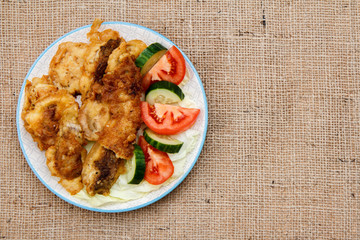 Plate with pieces of fried fish and freshly sliced tomatoes and cucumbers. Top view