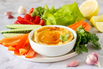 Hummus, different vegetables and lettuce leaves with lemon and garlic on a light background. Vegan food.