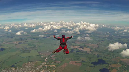 Afwasbaar Fotobehang Luchtsport Skydiver in een rode jumpsuit in vrije val boven de wolken