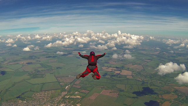 Skydiver in a red jumpsuit freefalling above the clouds