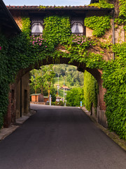 Fototapeta premium Biella, Italy, June 10, 2018 - Old house, walls covered with ivy and arch connecting the second part of the house with road below, Italy