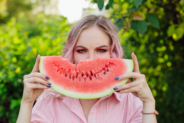 Beautiful young woman with pink hair holding juicy watermelon close to the face