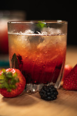 Bonito cóctel con zarzamoras, fresas y hojas de menta en un bonito vaso de vidrio sobre un fondo de madera