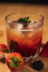 Bonito cóctel con zarzamoras, fresas y hojas de menta en un bonito vaso de vidrio sobre un fondo de madera