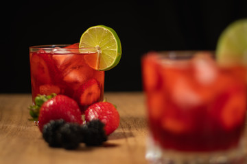 Bonito Cóctel con fresas, zarzamoras y una rodaja de limón para adornar en un fondo negro y de madera