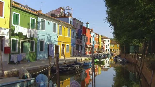 Walking over a narrow calm channel running through the vivid streets of Venice. Picturesque view of the colorful houses in the city streets of Burano, Italy. Breathtaking Venetian houses in summer.
