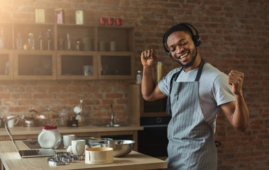 Happy black man listening to music and dancing in kitchen