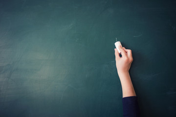 children's hand writes chalk on green blackboard in classroom