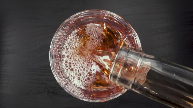 In a beautiful crystal glass on a black background pouring rose wine from a bottle top view