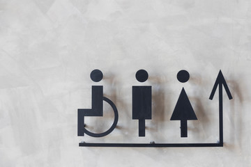 mens and womens disabled restroom signage with arrow made from steel plate on grey concrete wall.