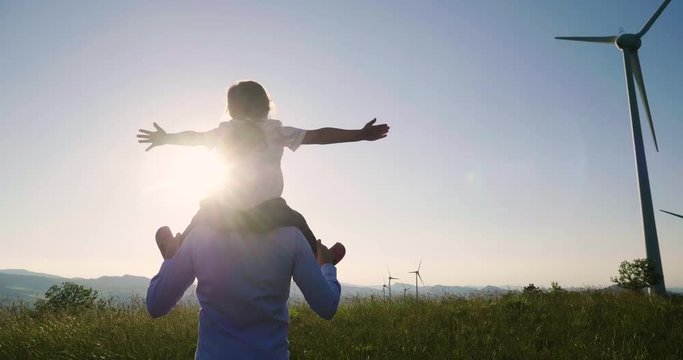 A father engineer holds his daughter in his arms and runs between the wind turbines with great freedom. Concept of: environmental engineering, renewable energy and love for nature and for the family
