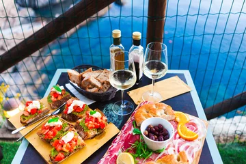 Fototapeten Romantic dinner for two at sunset. White wine and Tasty italian snack: fresh bruschettes  and meat on the board in outdoor cafe with amazing view in Manarola © yatcenko