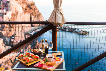 Romantic dinner for two at sunset. White wine and Tasty italian snack: fresh bruschettes  and meat on the board in outdoor cafe with amazing view in Manarola - 209889373