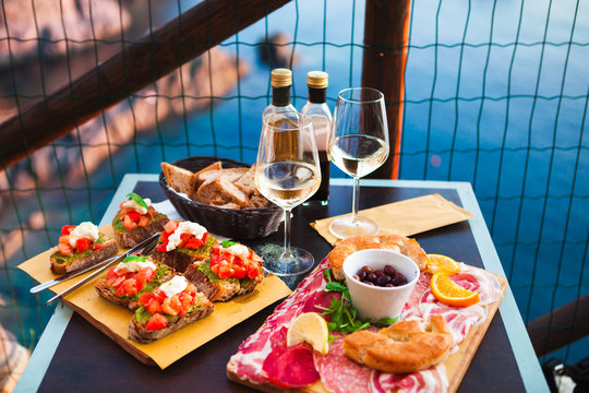Romantic dinner for two at sunset. White wine and Tasty italian snack: fresh bruschettes  and meat on the board in outdoor cafe with amazing view in Manarola