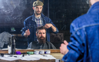 Man with beard and mustache in hairdressers chair in front of mirror background. Hipster client...