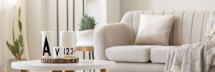 Close-up photo of white vessels standing on white end table in bright living room interior with...