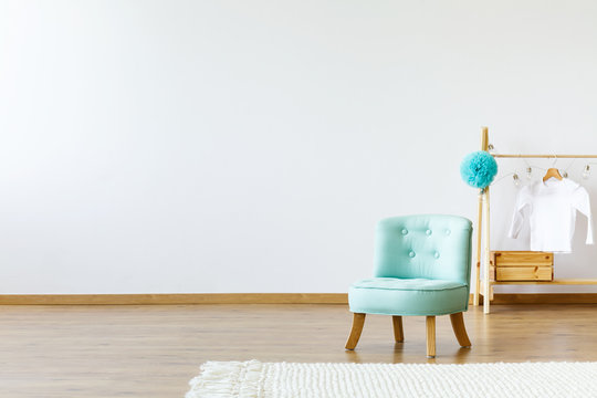 Mint chair, wooden hanger with a T-shirt on pompom and rug on an empty wall. Place your product