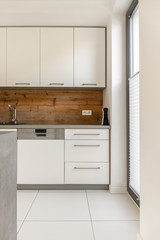 Real photo of an elegant, white kitchen interior with wooden panels on the wall and white cupboards
