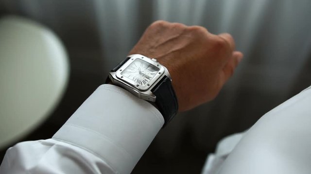 The elegant man is cheking time. He is wearing the luxuty silver watch with brown leather buckles. No face.