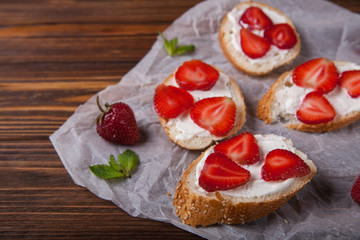 Toasts or bruschetta with strawberries on cream cheese on wooden background. Top view. Copy space