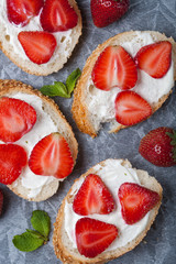 Toasts or bruschetta with strawberries on cream cheese on black background. Top view. Copy space