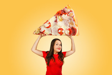 Cute funny young girl holds over herself huge piece of pizza with cheese on orange background