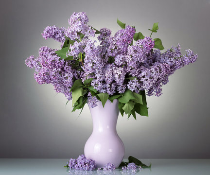 Charming bouquet of blooming lilac in vase on grey