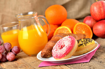 Sweet breakfast, donuts, orange, grapes, apples and orange juice on wooden table