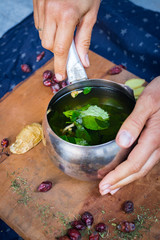 Woman hands holds herbal mint tea with ginger. Morning light and breakfast. Natural hot warning refreshing tea boiled in steel pot with rose hip dried berries. Carrier of vitamins and good health