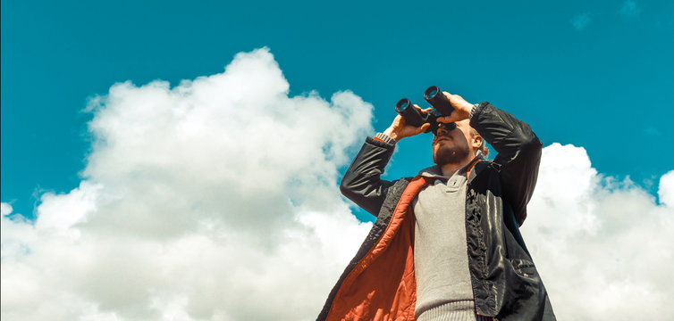 Travel Search Concept. Strong Traveler Man Looking Through Binoculars In The Distance Overview Sky. Low Angle Point Shoot