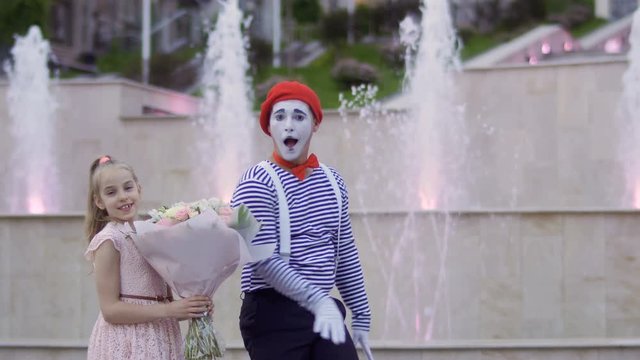 Funny mime and little girl with bouquet of flowers at background of fountains