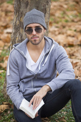Fototapeta premium Handsome man in nature reading a book. Autumn leaves. Copy space