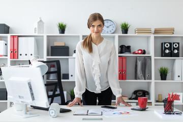 A young girl is standing right next to a table in the office.