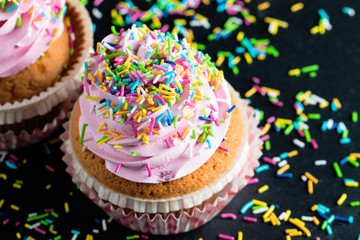 Closeup of cupcakes with vanilla, berries, pink and white cream, chocolate and sprinkles on wooden background. Selective focus. Sweet dessert tasty food concept muffin.