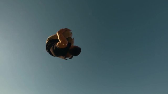 Muscular man performs extremely flip from the height at sunny day