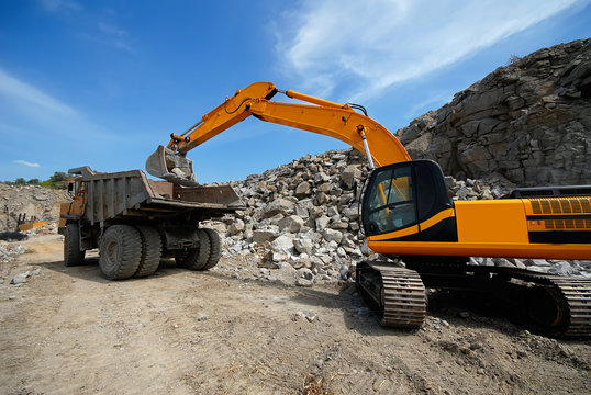 universal excavator loads granite stones in a dumper.