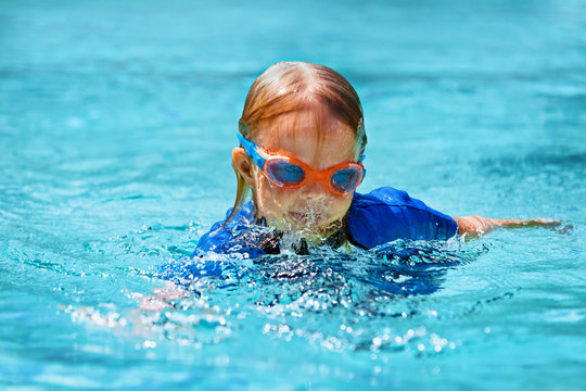 Happy child in wetsuit and goggles learn to swim, have fun in outdoor pool. Healthy family lifestyle, little kids water sports activity, swimming lessons with parents at training aqua classes.