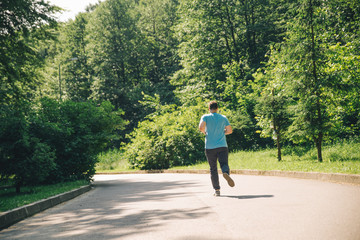 young adult man running at city park in sunny day. view from behind
