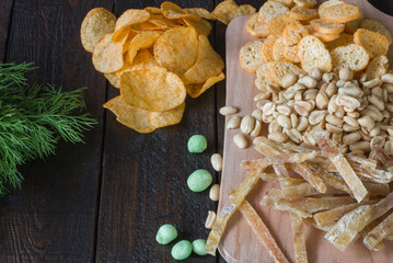 Snacks to beer, on a wooden board, on a wooden table. Chips, peanuts, pieces of fish,crackers, dill. Copy space. Close-up. The concept of junk food.