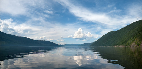 panorama summer Cumulus huge clouds in the blue sky and reflection in the lake. around the high mountains